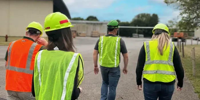 Field team in hard hats and hi-vis vests walking across an industrial yard