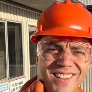 Sercan Esen wearing an orange hard hat and safety glasses at an industrial site