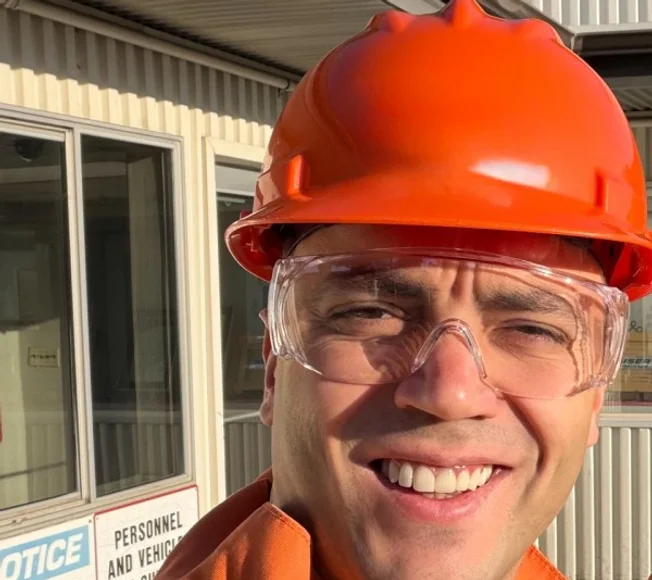 Sercan Esen wearing an orange hard hat and safety glasses at an industrial site