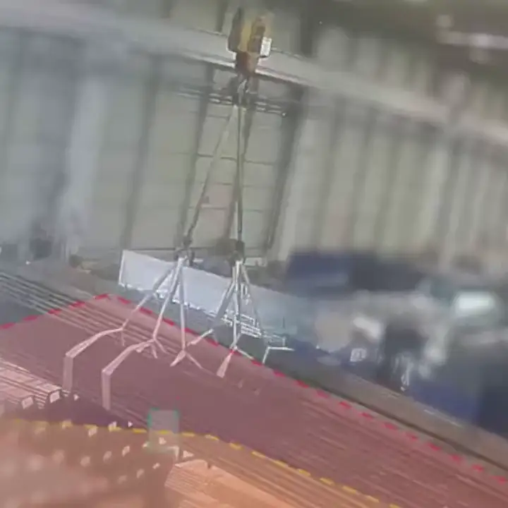 Overhead crane carrying bundled steel with the suspended-load area outlined in red below