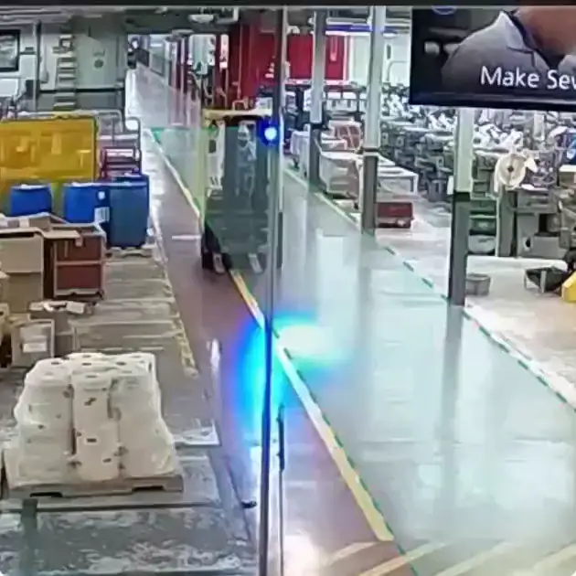 Forklift with a flashing blue warning light driving a marked aisle between production lines